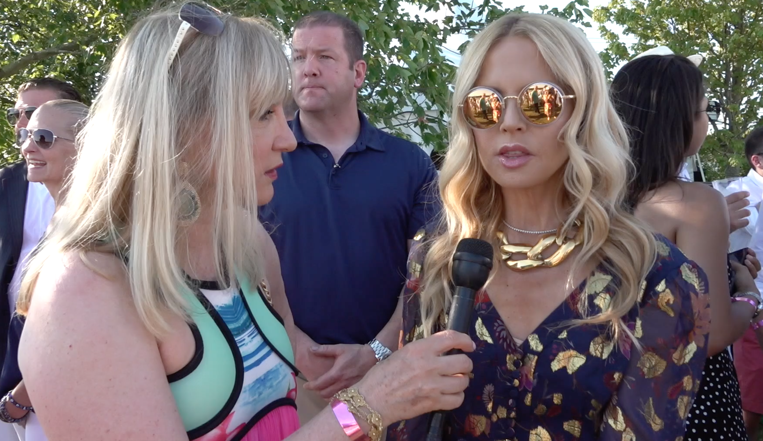 A woman in sunglasses talking to a reporter at an event.