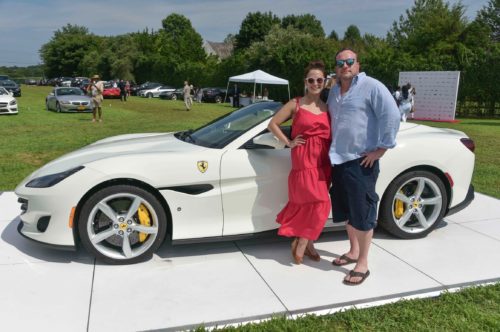 A man and woman standing next to a white ferrari sports car.