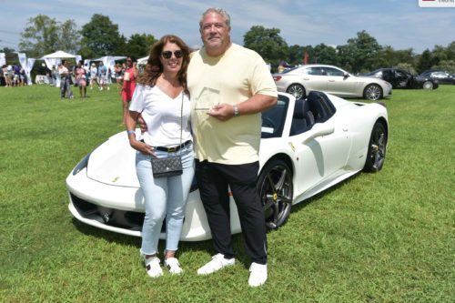 A man and woman standing next to a white sports car.