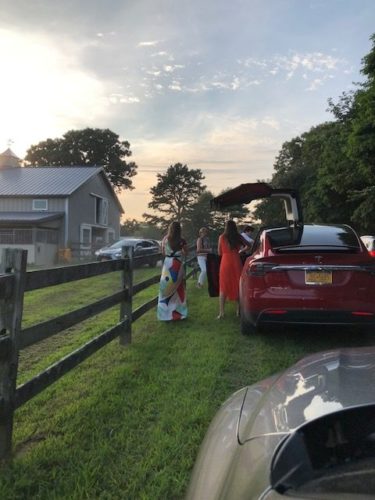 A group of people standing next to a red tesla model s.