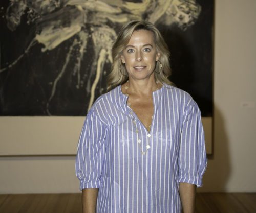 A woman in a blue shirt standing in front of a painting.