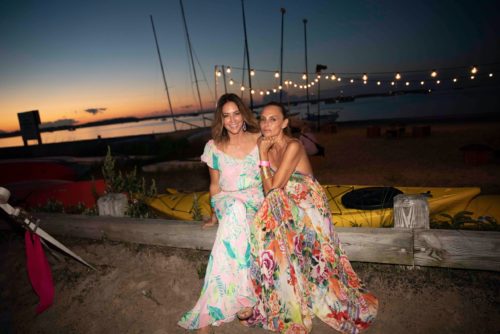 Two women in floral dresses posing on a dock at dusk.