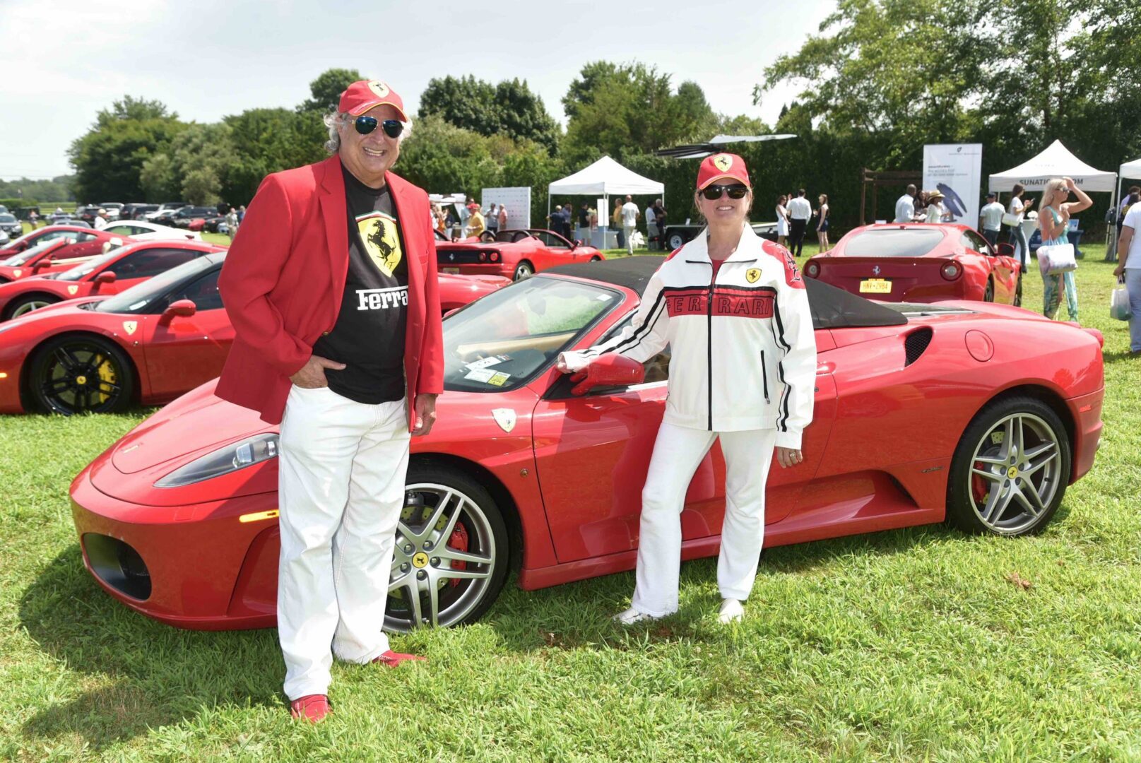 Two people standing next to a red ferrari sports car.