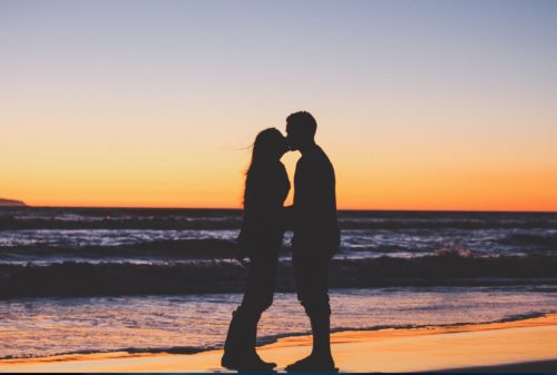 A couple kissing on the beach at sunset.