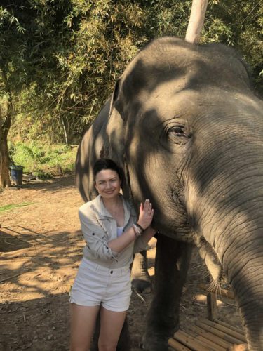 A woman is posing next to an elephant.