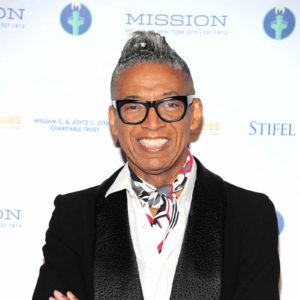 A man in a black suit and tie is standing on a red carpet.