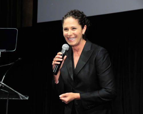 A woman in a black suit holding a microphone.