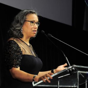 A woman in glasses giving a speech at a podium.