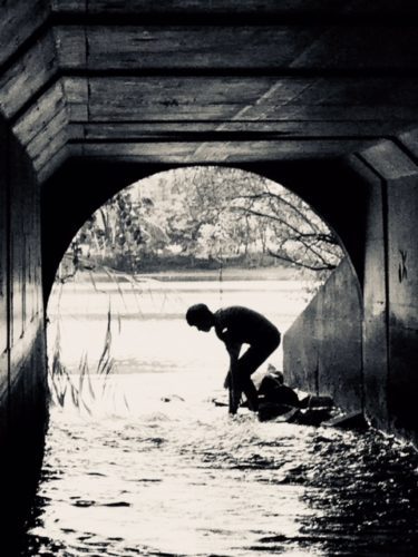 A man is standing in the water under a bridge.