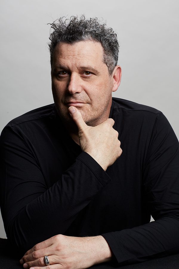 A man in a black shirt posing with his hand on his chin.