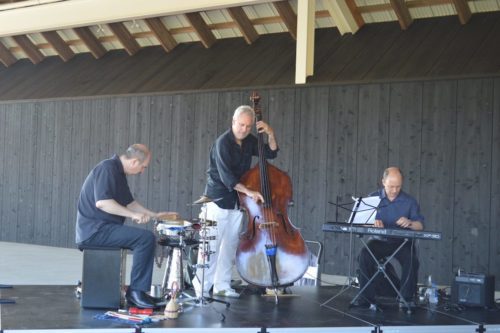 Three men playing music on a stage in front of a building.
