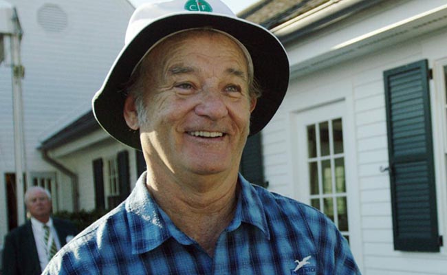 A man in a hat smiling outside of a house.