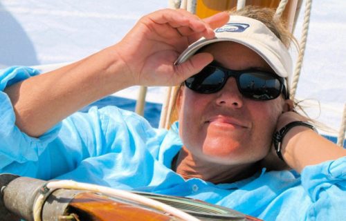 A woman wearing a hat and sunglasses on a sailboat.