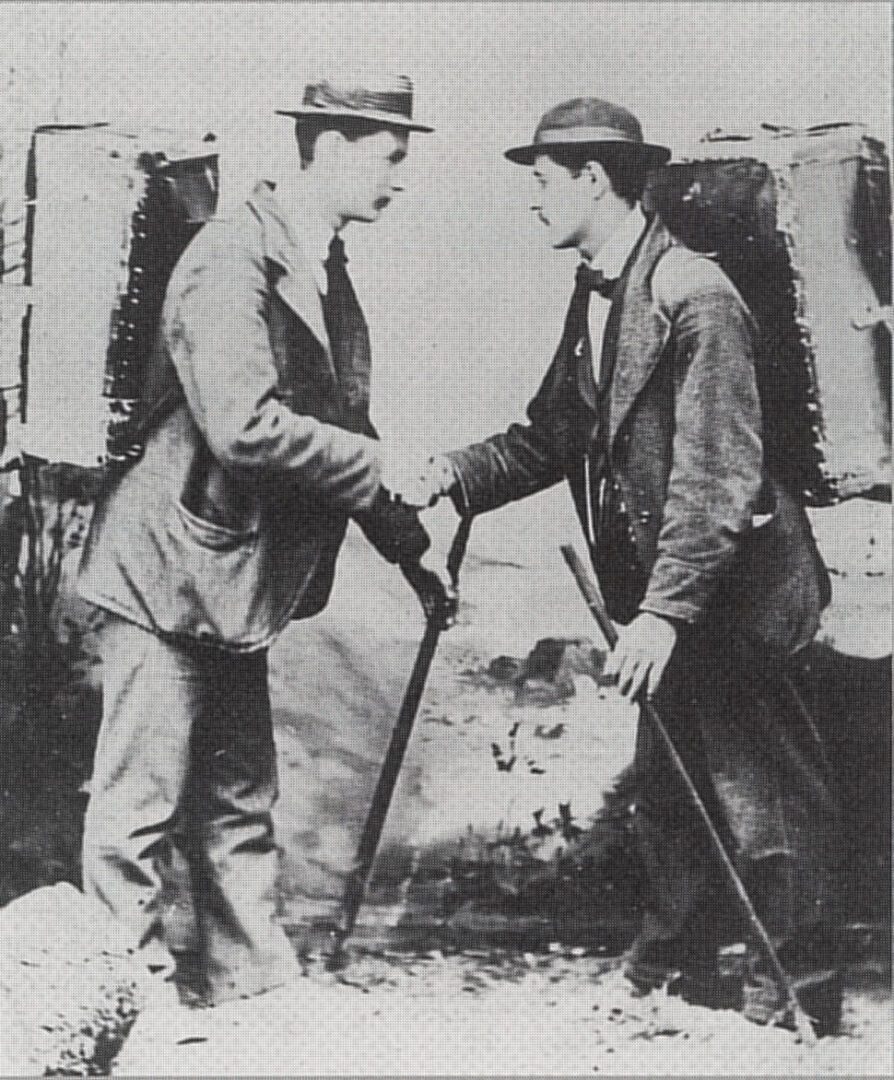 Two men shaking hands with suitcases on their backs.