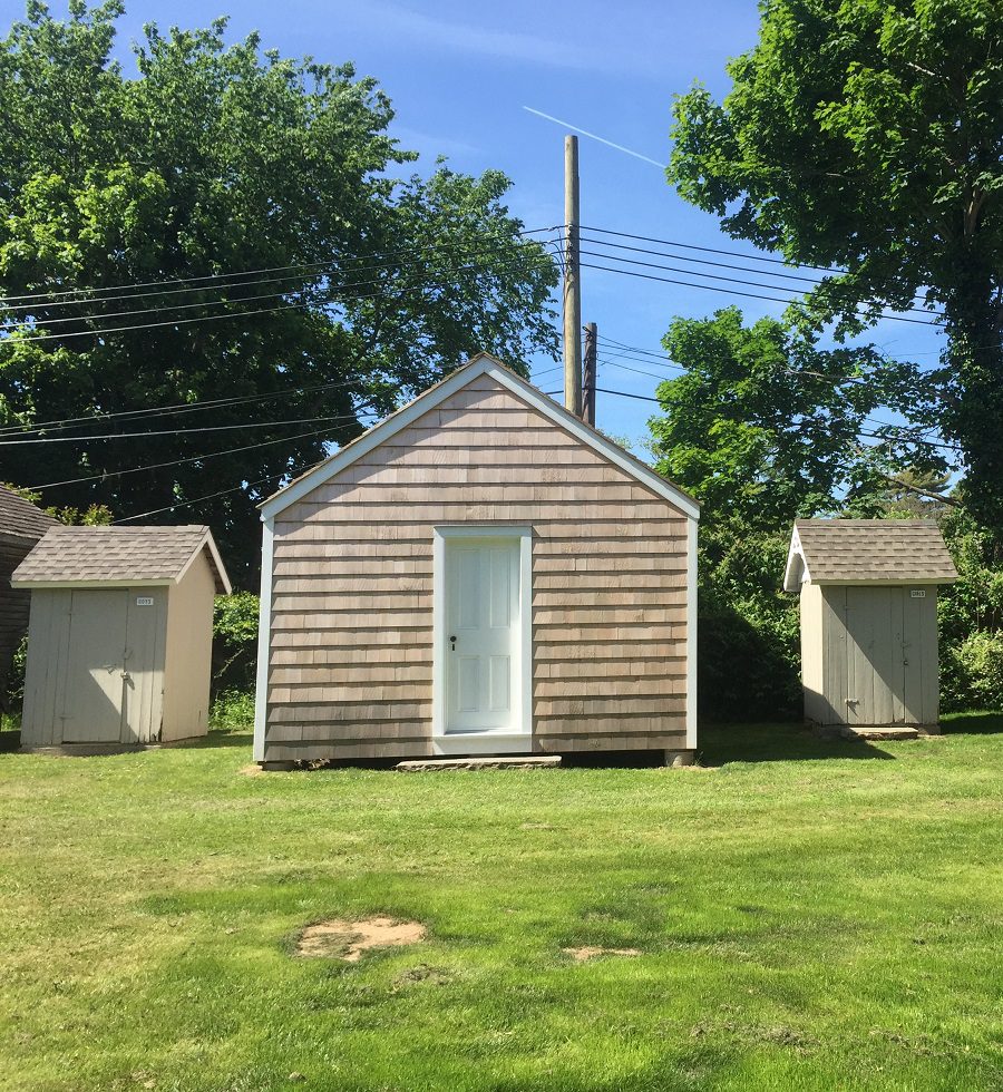 Three small sheds in a grassy area.