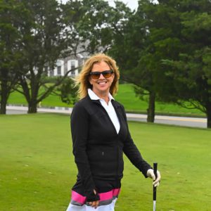 A woman wearing a black jacket and pink skirt on a golf course.