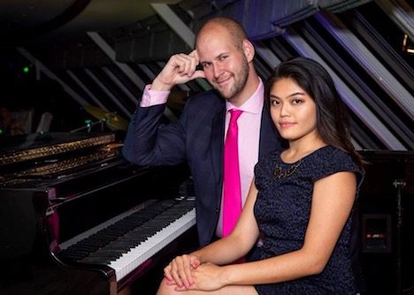A man and woman posing for a photo next to a piano.
