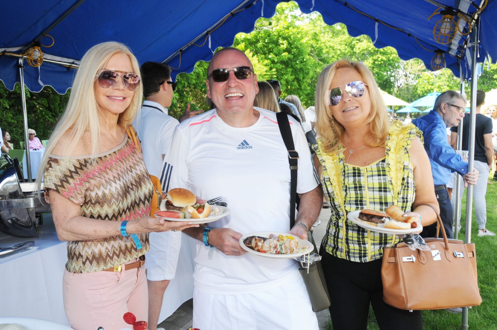 Three people standing under a tent with plates of food.