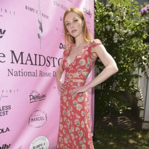 A woman in a floral dress standing in front of a pink banner.