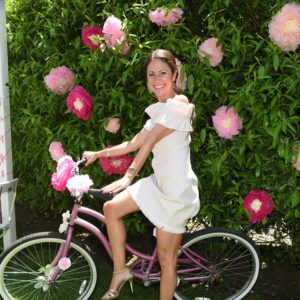 A woman in a white dress riding a pink bike.