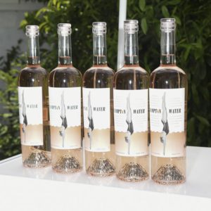 Five bottles of pink wine are lined up on a table.