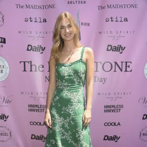 A woman in a green dress standing in front of a pink wall.