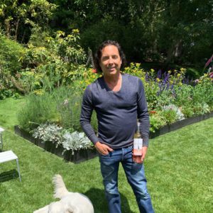 A man standing next to a dog in a garden with a bottle of wine.