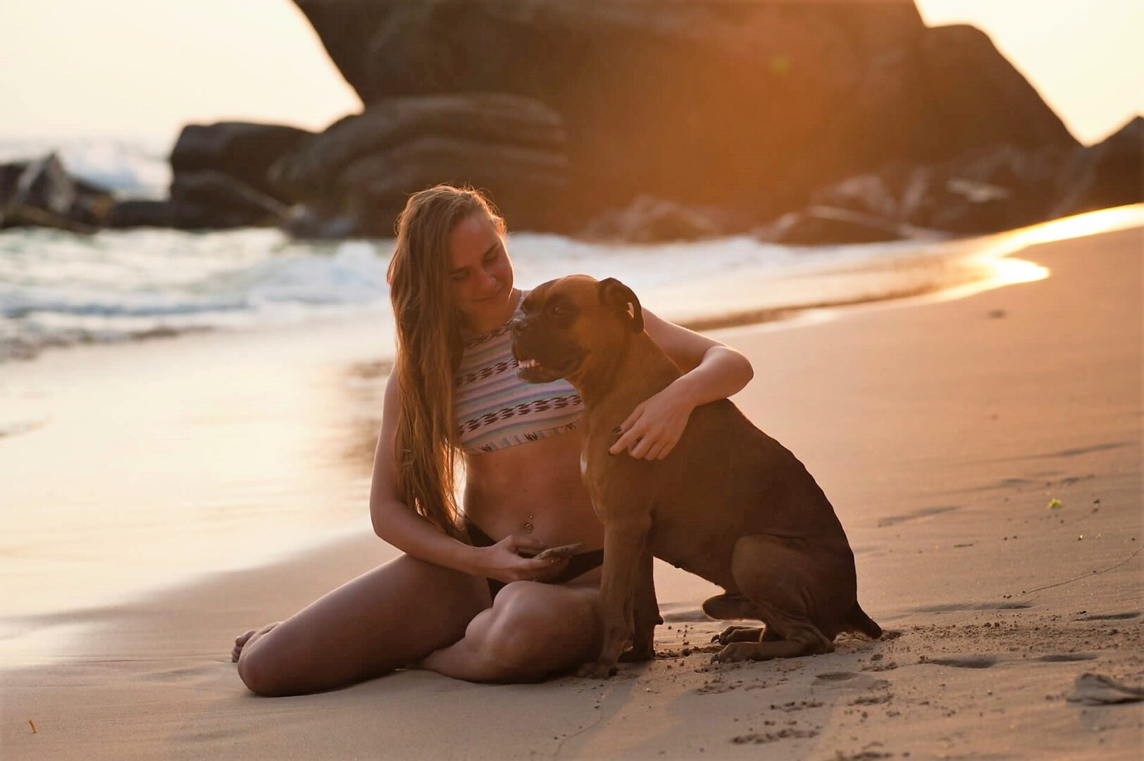 A woman sitting on the beach with a dog.