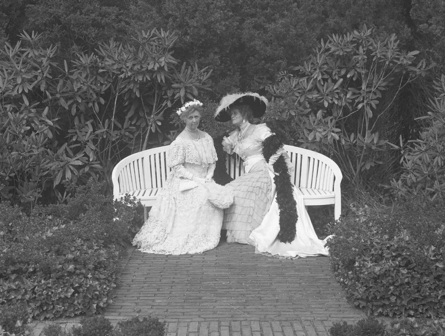 Two women sitting on a bench in a garden.