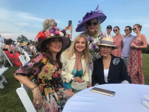Four women in hats posing for a photo at an outdoor event.