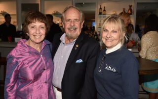 Three smiling adults posing indoors at a social event.