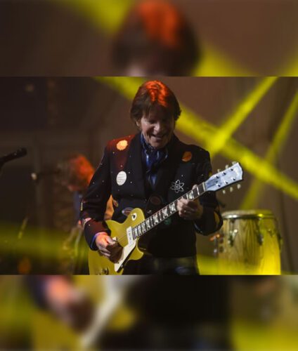 A man playing a guitar in front of a yellow light.
