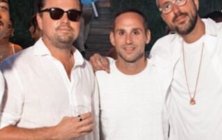 Three men posing together, all wearing white shirts, one with sunglasses.