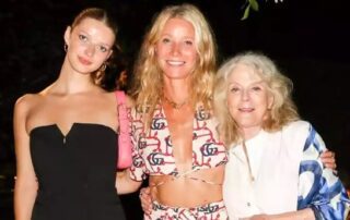 Three women posing together outdoors at night with greenery above.