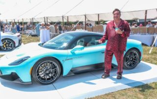 A man in pajamas standing next to a blue sports car.