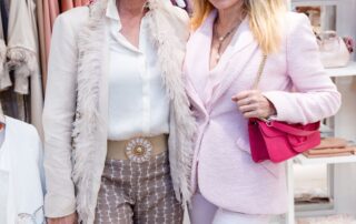 Two stylish women posing in a chic boutique with fashionable outfits.