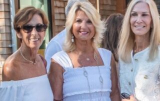 Three women smiling in white outfits.