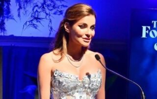 Woman in silver dress giving speech.