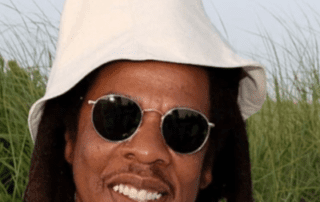 Jay-Z wearing a white bucket hat and sunglasses.