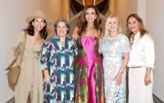 Five women in elegant dresses at a gallery.