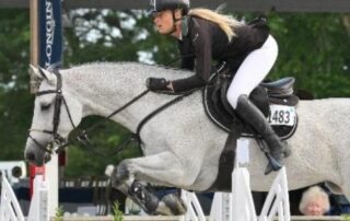 Woman jumping gray horse over hurdle.