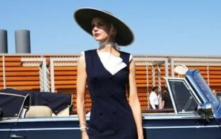 Woman in vintage dress and hat by car.