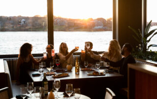 Group of friends toasting with drinks at sunset by the water.
