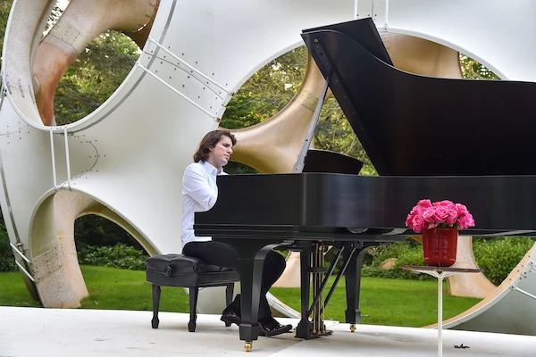 A man playing a grand piano outdoors in a modern artistic setting.