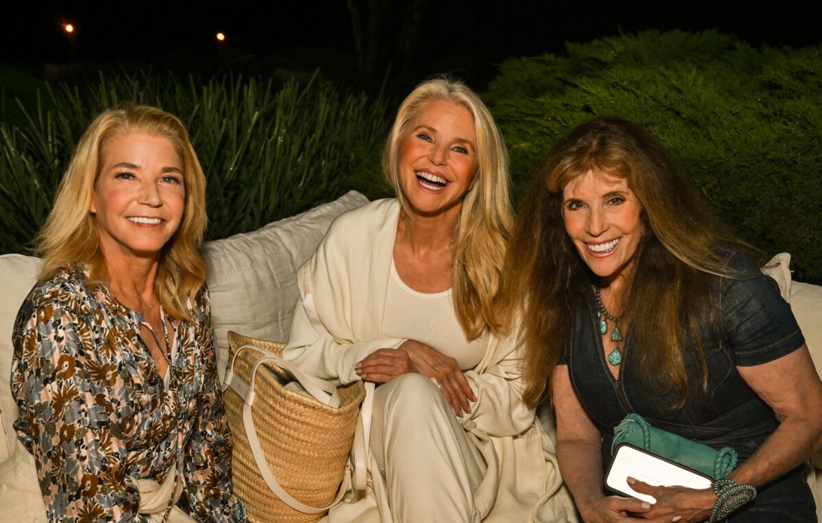 Three women sitting outdoors, smiling and enjoying each other's company at night.