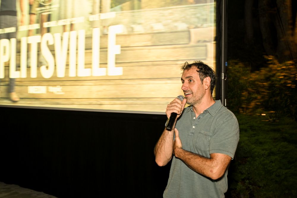 Man speaking into a microphone in front of a screen.