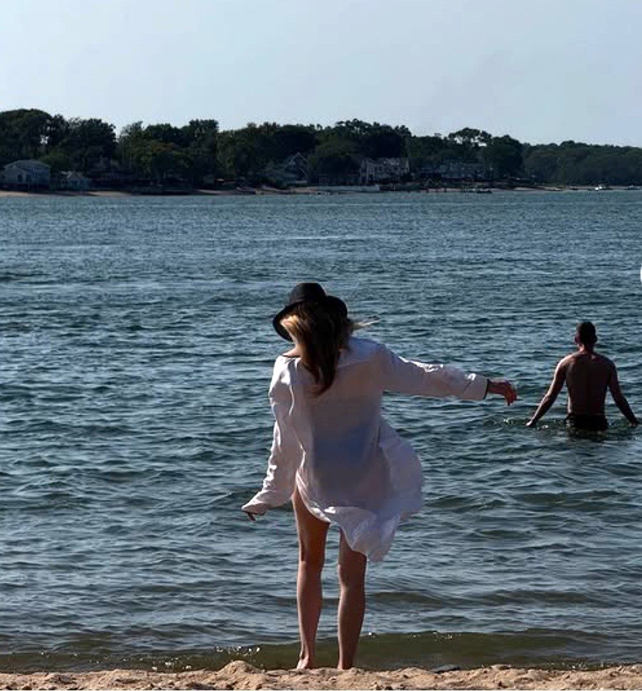 Person in a white shirt wading into a calm lake at sunset.