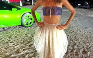 Woman in a stylish outfit posing outdoors near a green sports car at night.