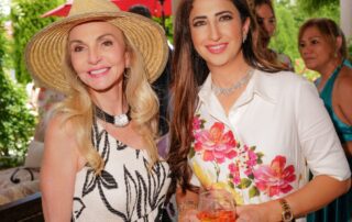 Two women smiling at an outdoor event, one holding a drink.