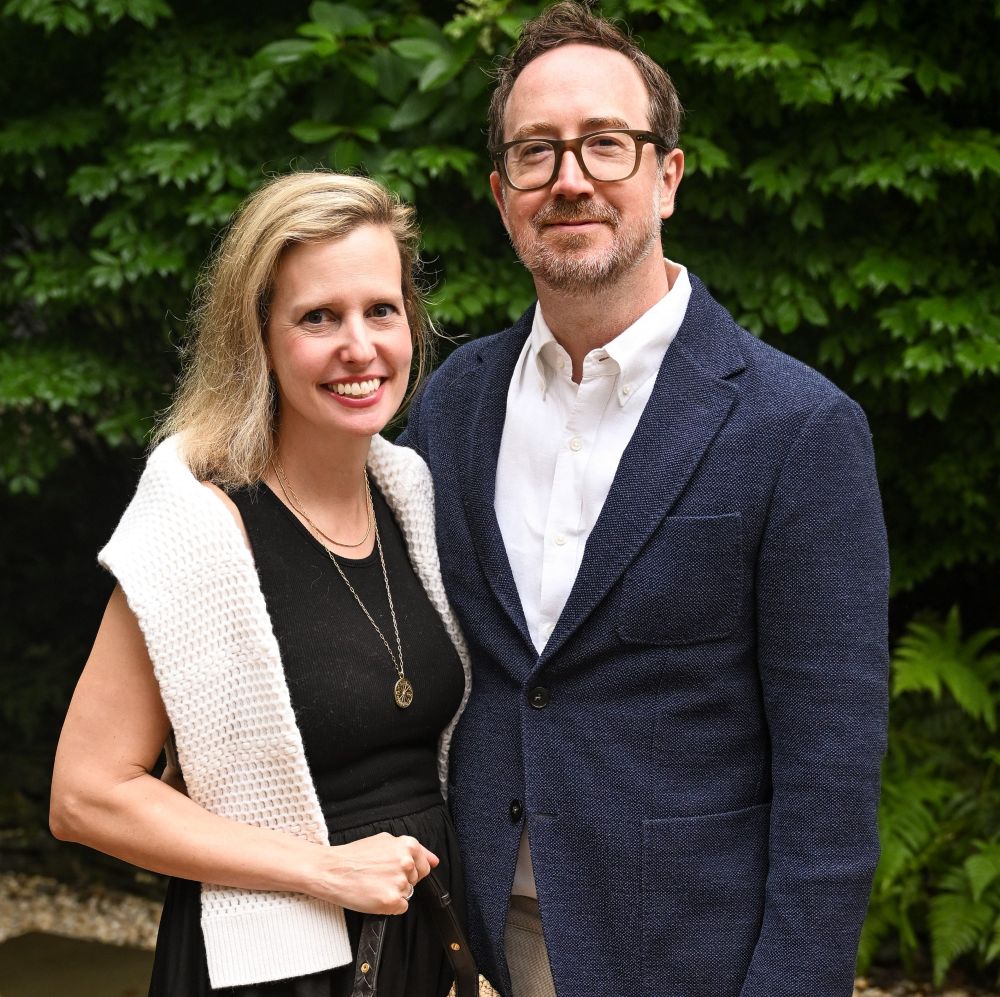A smiling couple posing outdoors with greenery in the background.